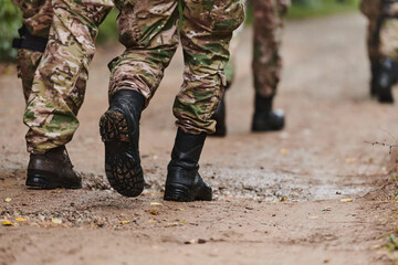 Close up photo, the resilient legs of elite soldiers, clad in camouflage boots, stride purposefully...
