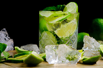 Mojito cocktail with ice, fresh mint and lime on a wooden board and black background close-up