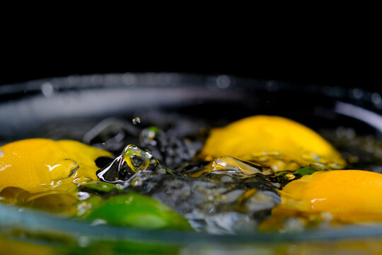 Ice cube falling into water with lemons on a black background and water splashes