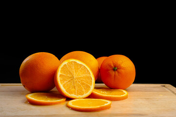 Composition with sliced ​​oranges on a wooden board on a black background.