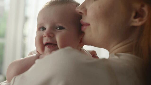 Child in mother arms, pleasure and happiness. Portrait, toddler looking over shoulder of woman mother. Concept of mother's love for baby child mother kisses child on cheeks head caresses beloved child