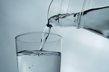 Water from jug pouring into glass on table, isolated on white background. clean water for a good health. Mineral water in glass. Image of clean water from nature.