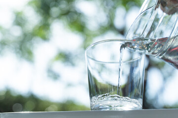 close up Water from jug pouring into glass on table in the morning, bokeh background. clean water for a good health. Mineral water in glass. Image of clean water from nature.