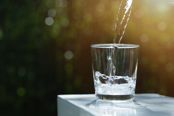 Water from jug pouring into glass on table in the morning, bokeh background. clean water for a good...