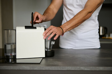 Details on hands of young man inserting a capsule with grinded coffee inside a coffee machine for home use