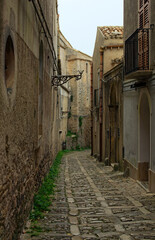 View of typical narrow pedestrian medieval cobblestone street along ancient buildings in historical part of Erice village, Sicily, Italy. Travel and tourism concept