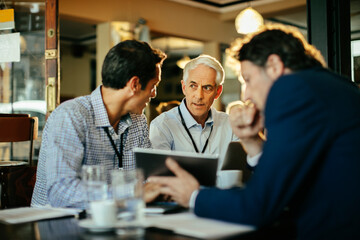 Business meeting in a cafe with three men discussing over a tablet