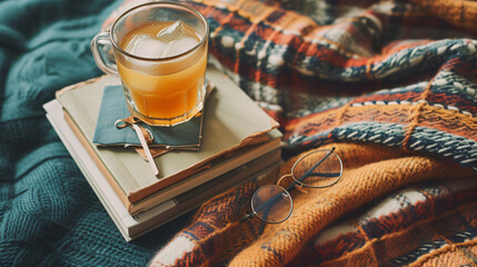 A flat lay of summer reading essentials including a stack of books reading glasses a bookmark and a cup of iced tea on a cozy blanket. - obrazy, fototapety, plakaty
