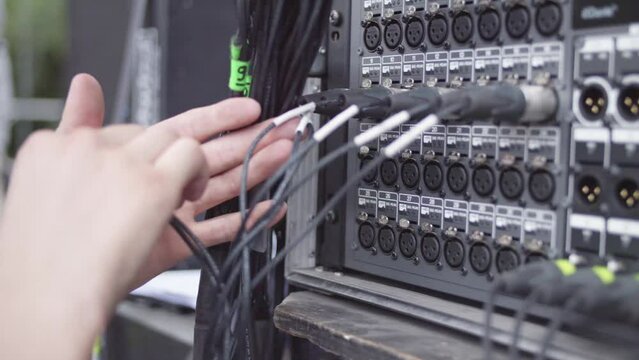 Close-up shot of hands plugging XLR cables into a multi-channel panel while setting up a stage for a concert.