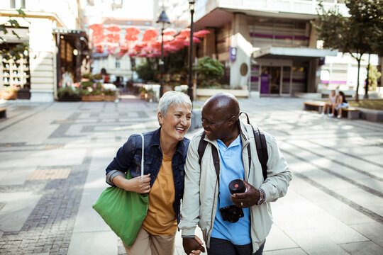 Happy senior interracial couple touring city with camera and shopping bag