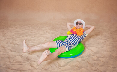 Comic funny man in vintage style striped swimsuit, colorful boa and sunglasses lying down on the inflatable ring