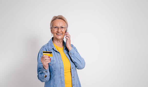 Smiling old female customer sharing credit card details on call over smart phone on white background