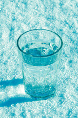 Pure spring water in a glass on white snow. Shadows in the snow