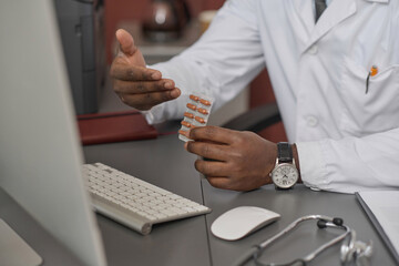 Hands of doctor showing medicine in capsules to computer webcam during video call with patient