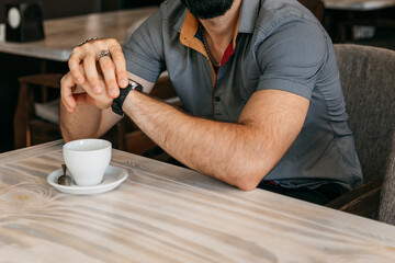A man is holding a watch while sitting in a cafe waiting for a friend.