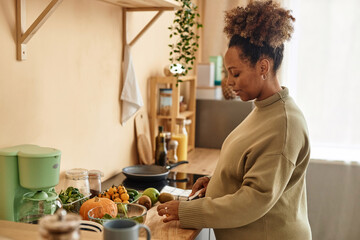 Fototapeta na wymiar Side view of pregnant young African American woman preparing meal on kitchen table from fresh ingredients
