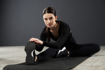 Beautiful focused woman stretching body, while leaning to leg before exercise on yoga mat. Front...