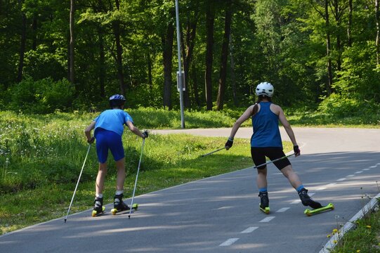 Teenagers at sports training roller skiing on an asphalt path on a summer day. Athletes in blue suits.