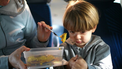 Mother feeding son during train trip. Child passenger being fed food while traveling. Mom holding...