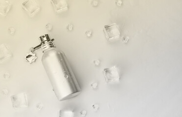 Naklejka premium Female perfume silvery bottle, Objective photograph of metallic perfume bottle in ice cubes and water on white table. View from above. Mockup product photo, concept of freshness and aroma