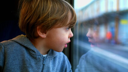One small boy traveling by train leaning on glass staring at view, reflection of child's face on...