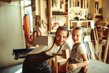 Fototapeta na wymiar Father carpenter taking selfie with daughter in workshop