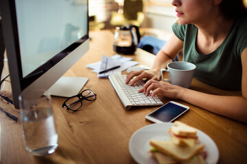 Freelancer working on computer with breakfast sandwich on desk