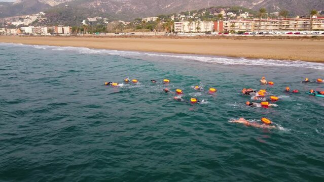 Swimmers in orange safety floats training in the sea near Castelldefels Beach, Barcelona, aerial view