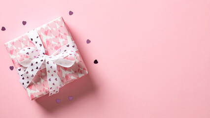 Pink gift box with white ribbon bow and heart shaped confetti on pink background. Top view with...