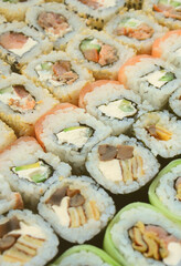 Close-up of a lot of sushi rolls with different fillings lie on a wooden surface. Macro shot of cooked classic Japanese food with a copy space.