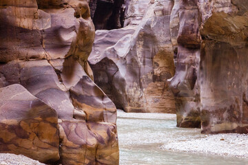 Jordan. Miracle of nature - Wadi el-Mujib gorge. Mesmerizing beauty of multi-colored steep cliffs of canyon. Along bottom of narrow gorge, among rock formations, flows unusually beautiful river,.