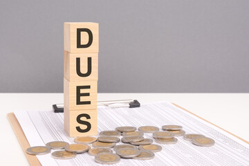 wooden cubes forming the text Dues, surrounded by coins, symbolize a commitment to financial...