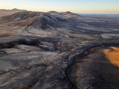 Golden hour light casts shadows over the ancient volcanic landscape along Fuerteventura's north coast, near El Cotillo and Majanicho, by Faro del Toston