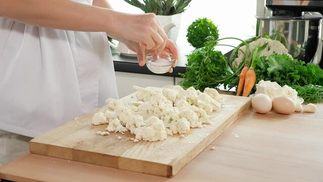 Woman preparing healthy vegan breakfast. A woman's hand sprinkles cauliflower with salt and mixes it with her hands on a wooden board, healthy food, home cooking, diet, diet food, vegetarian food, vit