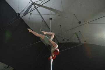 Low angle view of unrecognizable red-haired woman training pole dance elements hanging upside down...
