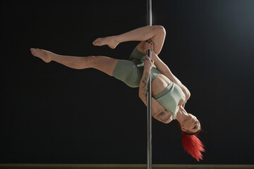 Full shot of skilled Caucasian woman in fitness wear performing outside leg hang trick holding and hooking one leg around pylon - Powered by Adobe