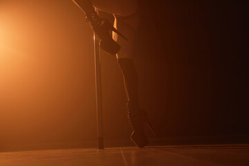 Unrecognizable female exotic dancer in black high-heeled shoes performing on stage in dark nightclub