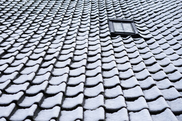 Old roof with roof tiles covered by snow and a small attic window