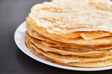 A round dish with fried pancakes on a brown table. A sweet dessert for breakfast. Sunny morning.