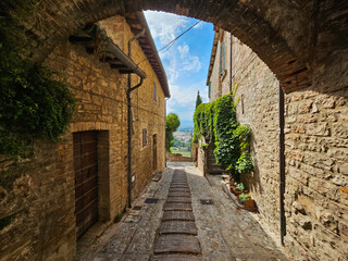 Picturesque view down an alley with green plants and a blue sky in Spello, the Province of Umbria, Italy.