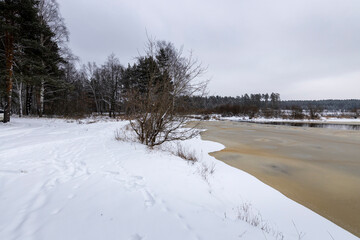 Footprints in the snow near an ice-covered river, trees along the shore