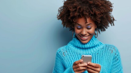 young woman with a vibrant afro hairstyle is smiling and looking at her smartphone, wearing a cozy turquoise turtleneck sweater against a matching turquoise background