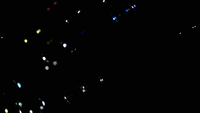 Stream Colorful Soap Bubbles, Light Bulbs Fly in Empty Space Black Background. Christmas lights. Many bright spotted bubbles float. Blurred motion, dark background. Focus. Bokeh. Night. Moving spots.