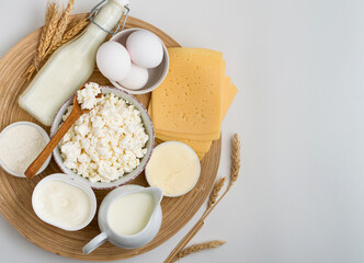Assortment of dairy products, milk, cottage cheese, cheese, cream cheese, butter, eggs and yogurt on a wooden stand on a light background. Horizontal, top view, for printing.