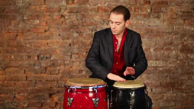 Man playing on two drums with thud sound near brick wall.