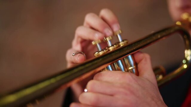 Fingers of man pushing button on trumpet close up.
