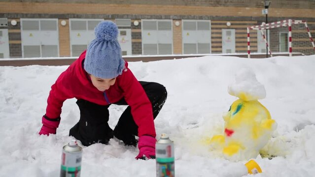 Girl taking in hand aerosol spray can in snow near small snow figure.