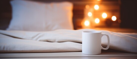 Bedside table with white mug against the bed at night time. - obrazy, fototapety, plakaty