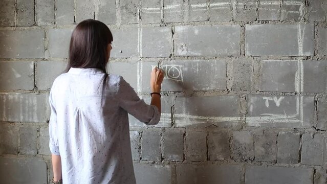Woman drawing two AC outlet in rectangle of future TV on bricked wall of flat