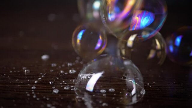 Close up, Lots of Colorful Stuck Together Soap Bubbles on a Brown Wooden Surface. Transparent rainbow bubbles with foam fly, connect, burst. Bubble bunch. Splash. Texture, structure. Blur. Abstract.